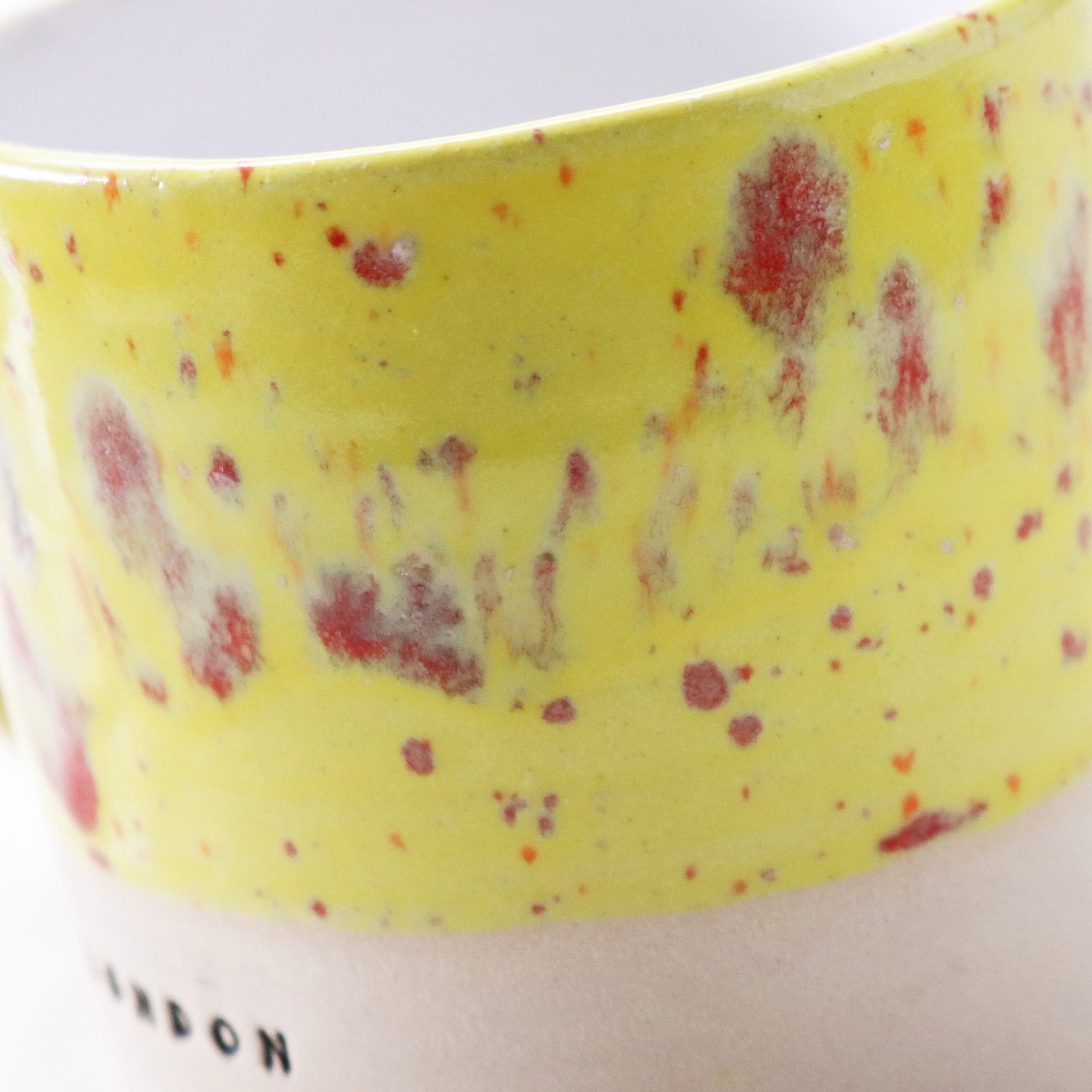 Ceramic mug in yellow with red flecks, stamped with ‘London’ – handcrafted by Lesley McShea