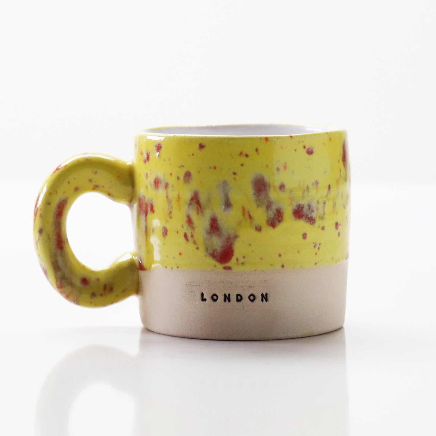 Ceramic mug in yellow with red flecks, stamped with ‘London’ – handcrafted by Lesley McShea