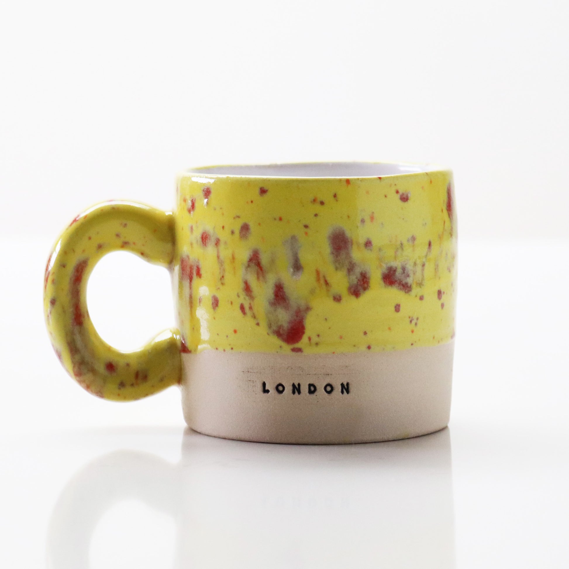 Ceramic mug in yellow with red flecks, stamped with ‘London’ – handcrafted by Lesley McShea